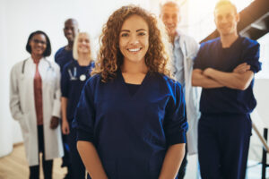 Smiling female doctor standing with medical colleagues in a hospital Smiling young female doctor standing in a hospital corridor with a diverse group of medical staff standing behind her