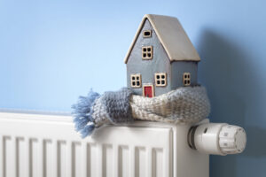 House model wrapped in scarf on radiator winter energy, heating and insulation background House model wrapped in scarf on radiator home winter heating and insulation background fuel and energy crisis concept